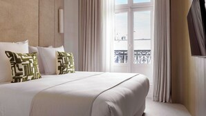 Ein Hotelzimmer mit einem großen Bett, Meerblick durch ein Fenster und einem Balkon mit Geländer.