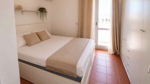 A bedroom with a bed, a window with curtains, an air conditioning unit, and a door. - Beautiful apartment with sea views (Cannigione)