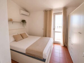 Ein Schlafzimmer mit Bett, einem Fenster mit Vorhängen, einer Klimaanlage und einer Tür.