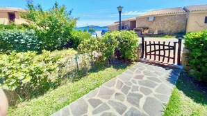 A stone pathway leading to a gated entrance with a lamp post, surrounded by greenery and buildings with terracotta roofs. - Beautiful apartment with sea views (Cannigione)