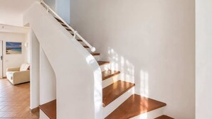 A curved staircase with wooden steps and white walls, leading to a room with a beige sofa and a beach-themed picture on the wall. - Beautiful apartment with sea views (Cannigione)
