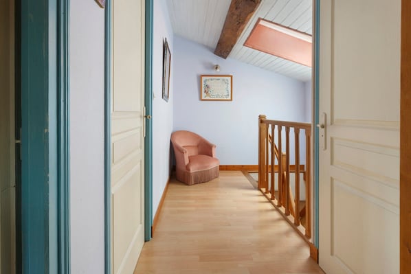 A narrow hallway with wooden flooring, a pink chair, and a wooden railing.