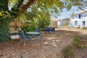 An outdoor seating area with a table and chairs, surrounded by trees and a stone wall.