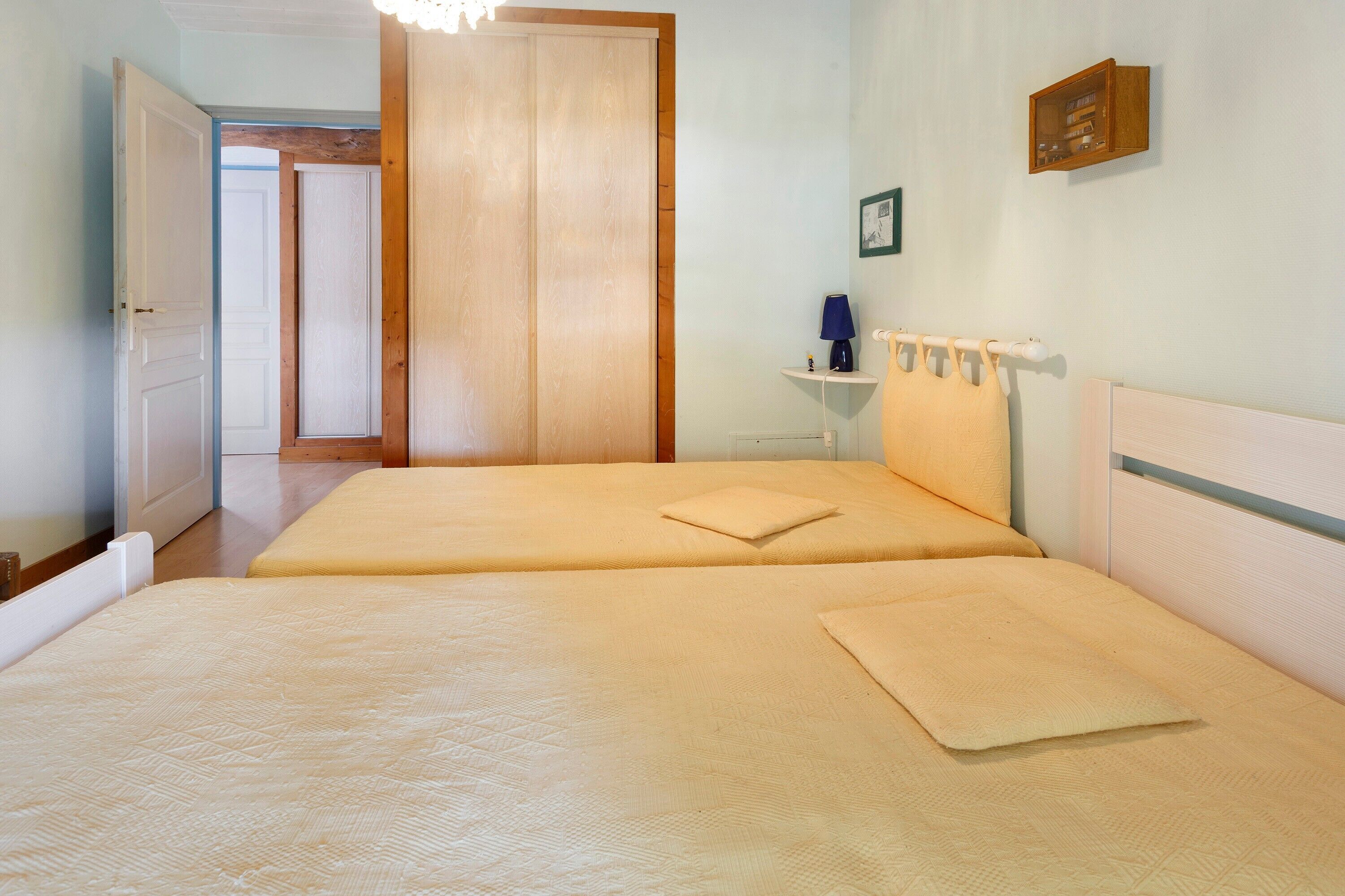 Een kamer met twee bedden, een klein nachtkastje met lamp, een wandplank en een deur naar een andere kamer.