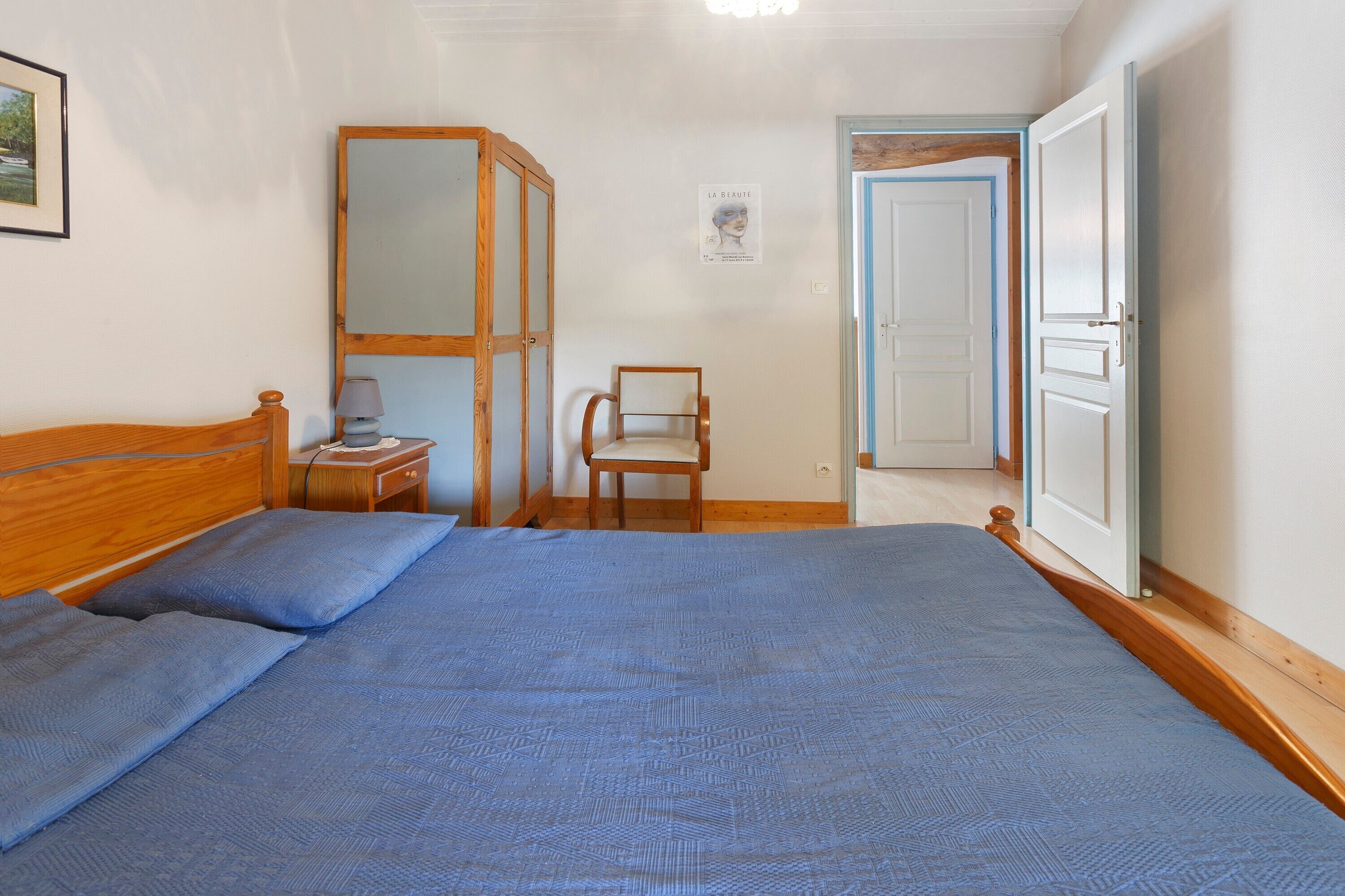 Un dormitori amb llit, cadira, armari i porta.