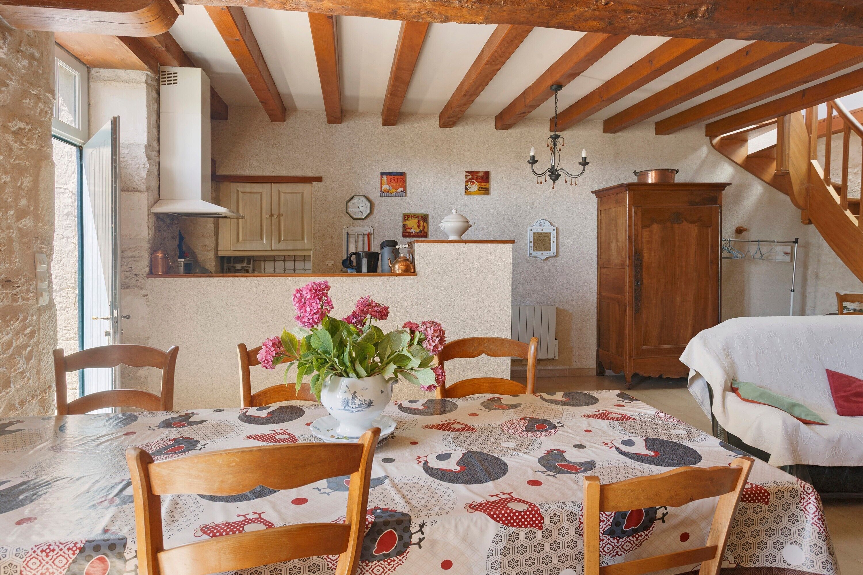 Una cocina rústica con vigas de madera, una mesa de comedor con mantel estampado y un jarrón con flores.
