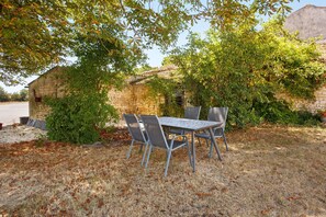 An outdoor seating area with a table and chairs, surrounded by greenery and a stone wall.