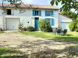 A white building with blue shutters, a garage, and a small patio with chairs. - Farm Cottage Between Oysters and Cognac (Antezant-la-Chapelle)