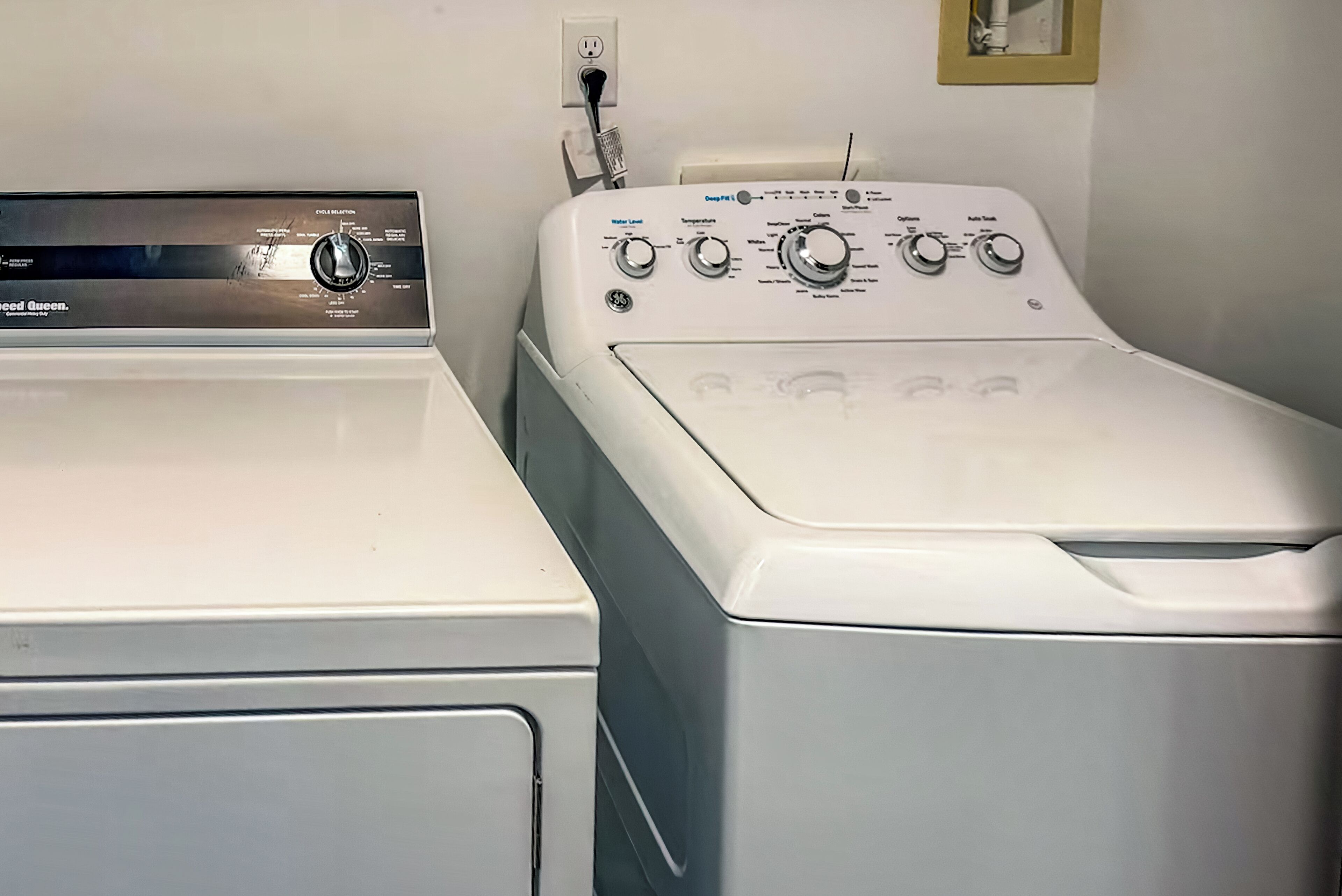 A front view of a laundry room with two washing machines, a water heater, and a power outlet.