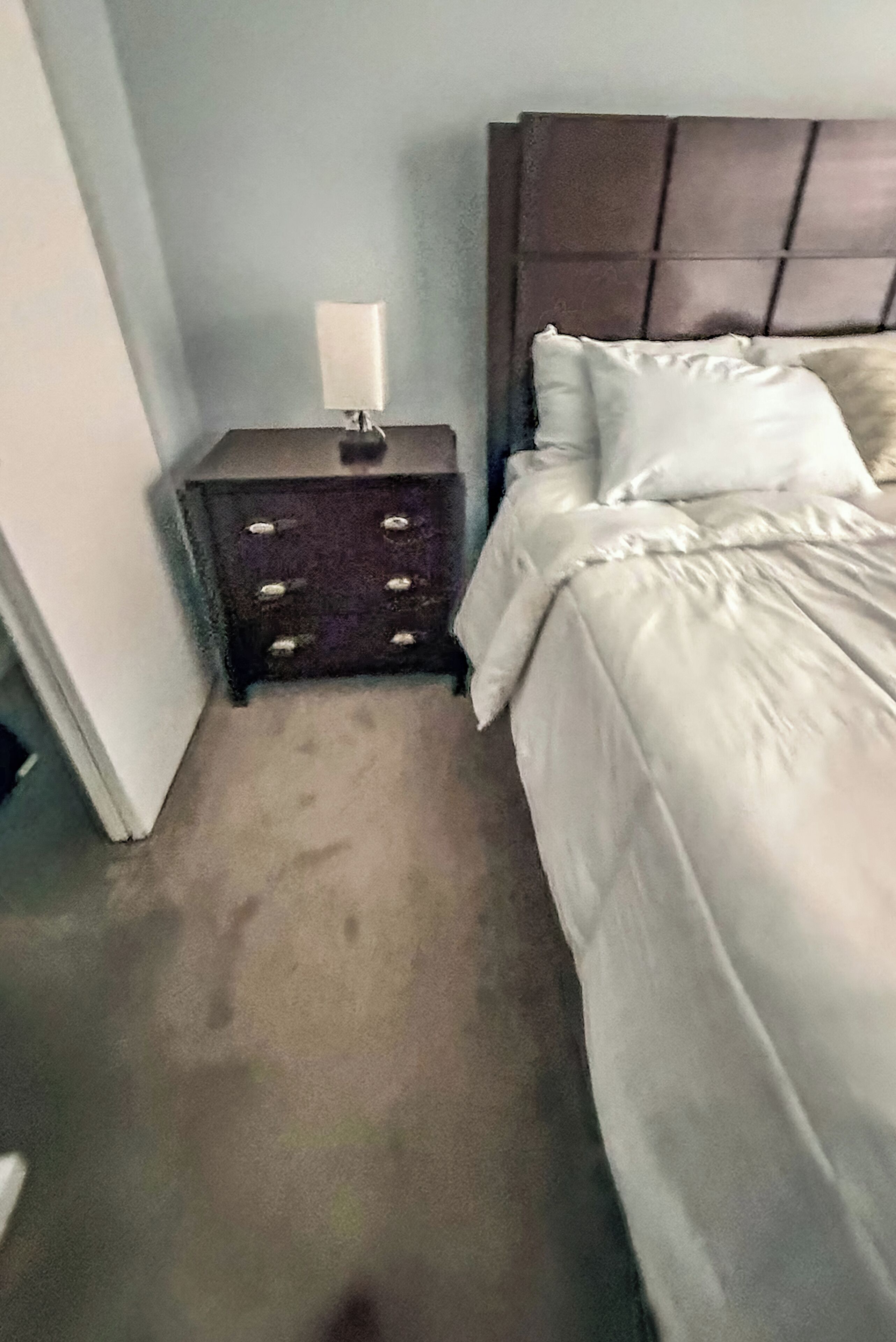 Un dormitorio con una cama, una mesita de noche con lámpara y un aparador.