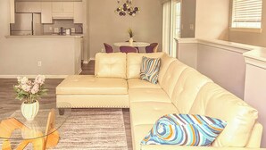 A living room with a beige sectional sofa, a glass coffee table, and a rug.