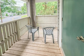 A wooden deck with two chairs and a railing, overlooking a street with houses and greenery.