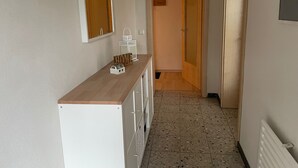 Un couloir avec un comptoir en bois, un miroir, une armoire blanche, une porte et un sol carrelé.