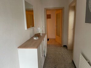 Ein Flur mit Holztresen, einem Spiegel, einem weißen Schrank, einer Tür und einem Fliesenboden.