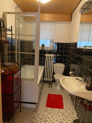Ein Badezimmer mit Dusche, Toilette, Waschbecken und Fliesenboden.