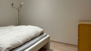 Une chambre à coucher au style minimaliste, avec un lit, une table de chevet en bois et un luminaire fixé au mur.