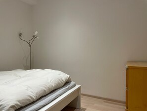 Ein schlicht eingerichtetes Schlafzimmer mit einem Bett, einem Nachttisch aus Holz und einer Wandleuchte.