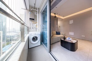 Un apartamento moderno con lavadora, sofá, mesa de centro y vistas a la ciudad a través de amplios ventanales.