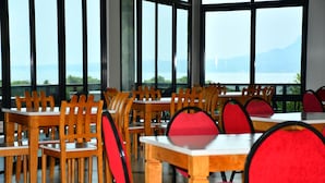Un restaurante con mesas y sillas de madera, ventanas amplias y vistas al agua.