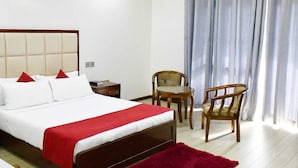 Habitación de hotel con cama, dos sillas, una mesita y ventana con cortinas.