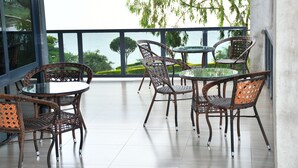Un balcón con mobiliario de mimbre y una mesa de vidrio, con vista a un cuerpo de agua y vegetación.
