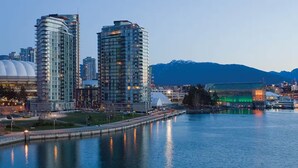 A waterfront cityscape with modern high-rise buildings, a bridge, and a mountain backdrop.