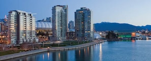A waterfront cityscape with modern high-rise buildings, a bridge, and a mountain backdrop.