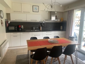 A modern kitchen with white cabinets, a black countertop, and a dining area with a wooden table and black chairs. - Vacation apartment near the beach in a vacation park, sports fields, pet-friendly (De Haan)