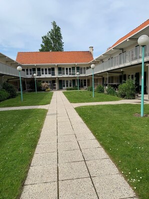 A building with a central courtyard, a covered walkway, and a red-tiled roof. - Vacation apartment near the beach in a vacation park, sports fields, pet-friendly (De Haan)