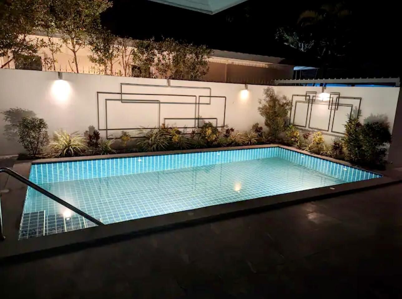 An outdoor swimming pool with a tiled floor and a metal railing.