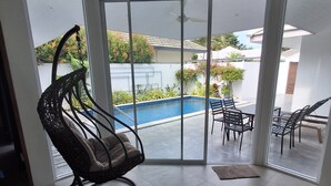 A room with a large sliding glass door leading to an outdoor area with a pool, a rocking chair, and a dining set. - 2-Bedroom Villa with 2 BTHR, Private Pool, Quiet Beach Just 2-Minute Walk Away (Koh SamuiProvince)