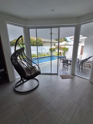 Ein Zimmer mit einer großen Schiebetür zu einem Außenbereich mit Pool, Schaukelstuhl und Esstisch.