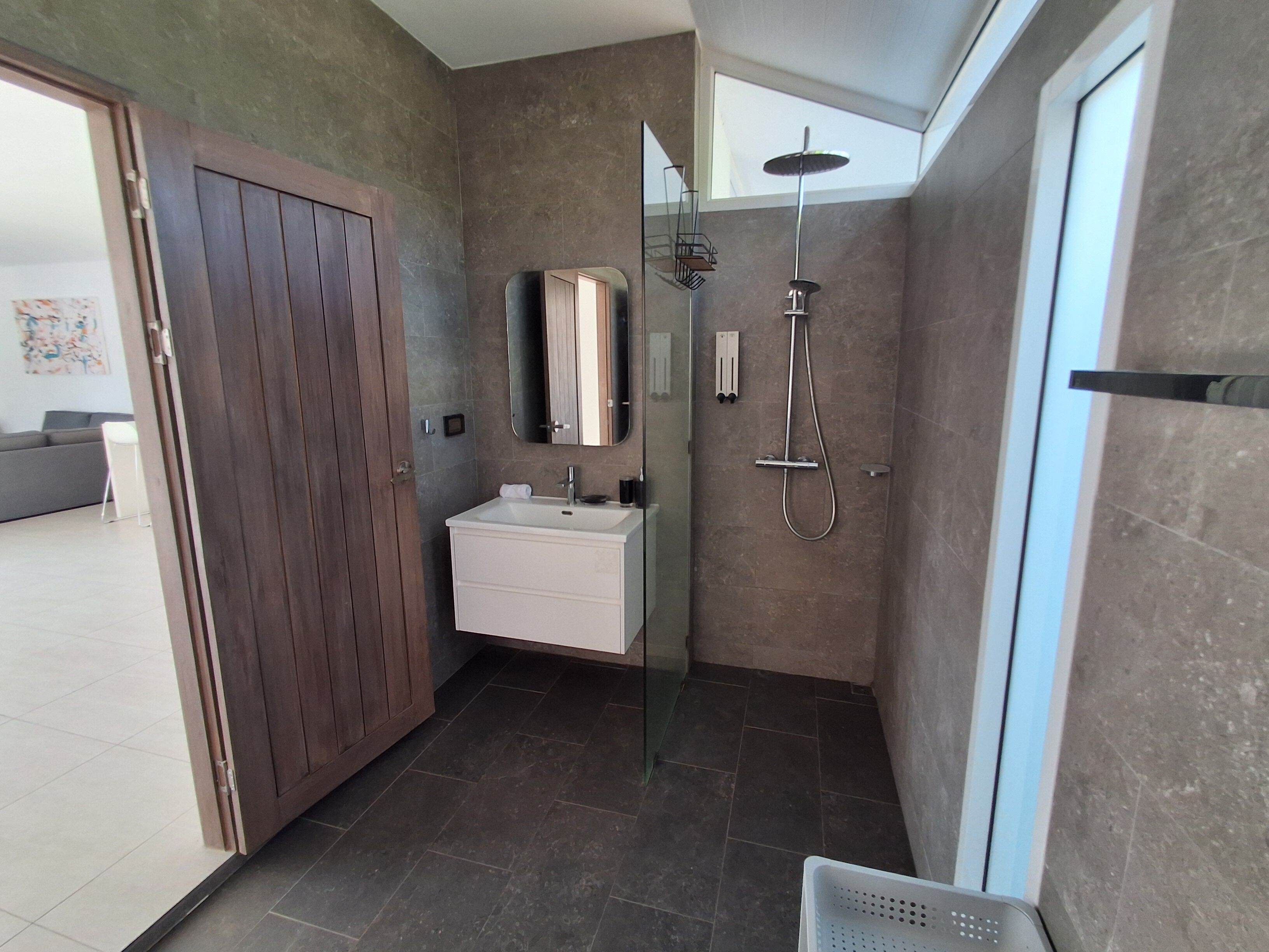 A modern bathroom with a glass shower enclosure, a white sink, and a wooden wardrobe.