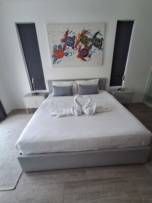 Una camera da letto moderna con un letto grande, biancheria da letto grigia e un quadro astratto colorato sopra.