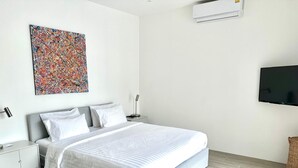 A modern bedroom with a large bed, a flat-screen TV, a wall-mounted air conditioner, and a colorful abstract painting. - 2-Bedroom Villa with 2 BTHR, Private Pool, Quiet Beach Just 2-Minute Walk Away (Koh SamuiProvince)