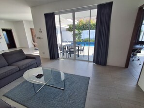 A modern living room with a sofa, a glass coffee table, and a view of an outdoor patio with a pool.