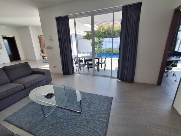 Un soggiorno moderno con un divano, un tavolino in vetro e vista su un patio esterno con piscina.