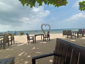 Ein Sitzbereich am Strand mit Holzsesseln und -tischen, einer herzförmigen Dekoration und Blick aufs Meer.