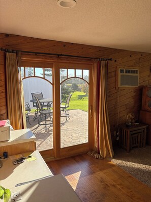 A room with a wooden floor, a desk with office supplies, a chair, and a view of an outdoor patio with chairs and a table.
