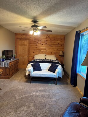A bedroom with a bed, a dresser, a chair, a ceiling fan, and a window with curtains.