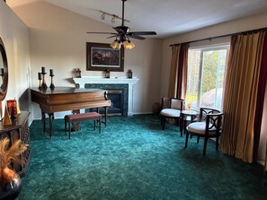 A room with a piano, chairs, a fireplace, and a large window with curtains. - Northern Oasis in the Warroad Estates (Warroad)