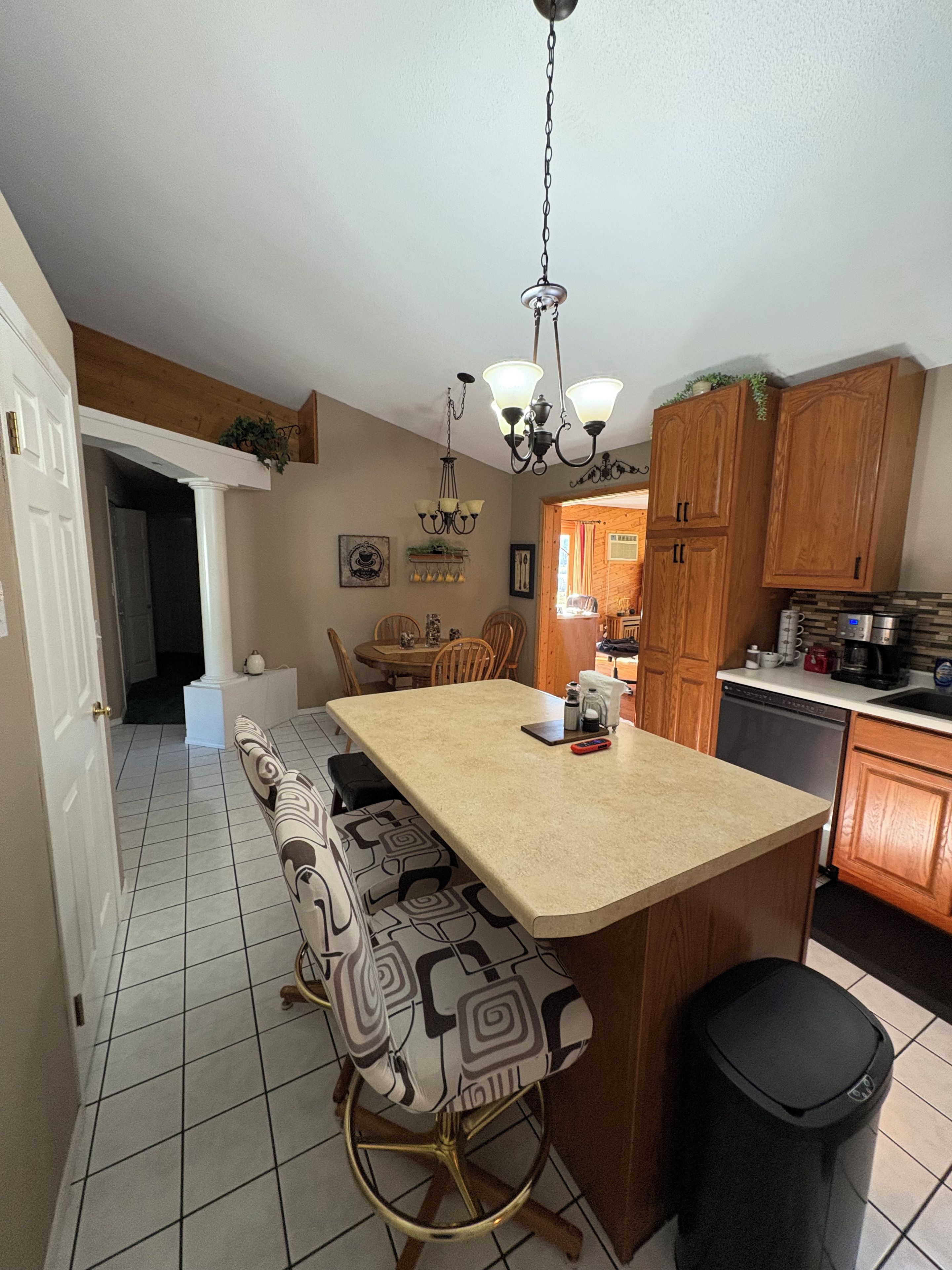 A kitchen with a central island, wooden cabinets, and a dining area with chairs.