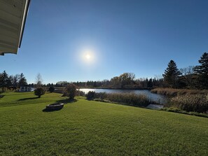 A grassy area with a pond, trees, and a clear sky.