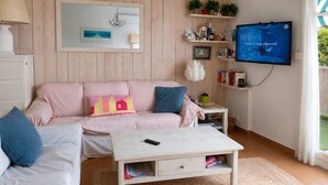 A living room with a sofa, a coffee table, a TV, and shelves with plants and books. - Seafront marina, a stone's throw from the beaches (Le Grau-du-Roi)