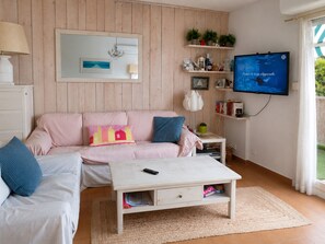 A living room with a sofa, a coffee table, a TV, and shelves with plants and books. - Seafront marina, a stone's throw from the beaches (Le Grau-du-Roi)
