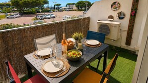 A balcony with a table set for two, a bottle, a bowl of salad, and a mirror on the wall. - Seafront marina, a stone's throw from the beaches (Le Grau-du-Roi)