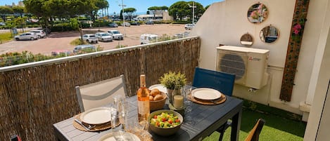 Un balcón con una mesa dispuesta para dos personas, una botella, un tazón de ensalada y un espejo en la pared.