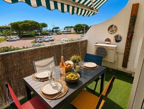 A balcony with a table set for two, a bottle, a bowl of salad, and a mirror on the wall. - Seafront marina, a stone's throw from the beaches (Le Grau-du-Roi)