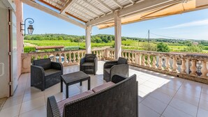 A covered outdoor seating area with wicker furniture, a tiled floor, and a view of green fields. - Large House with Private Pool in a Peaceful Setting – Pets Welcome (Valréas)