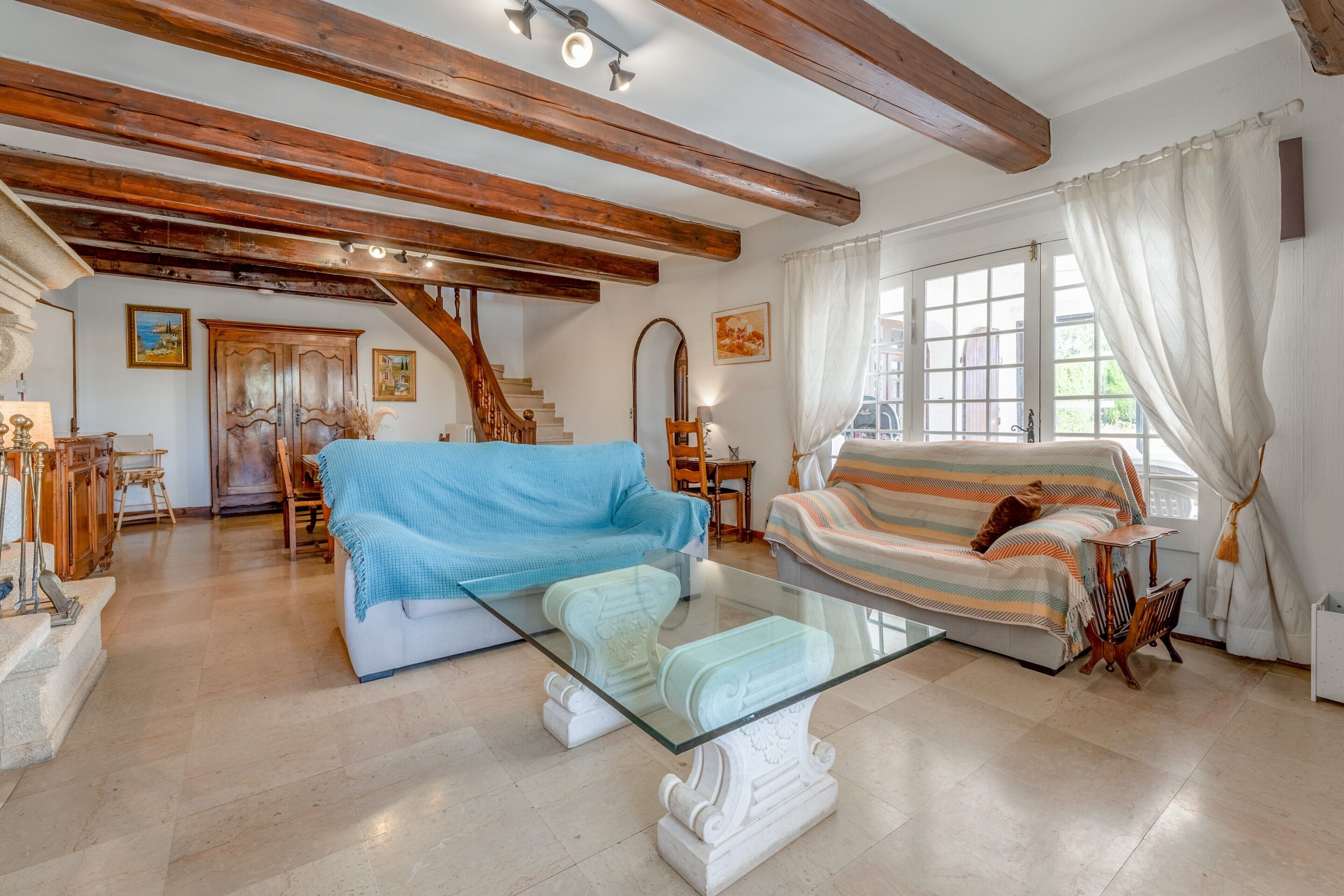 Ein geräumiges Wohnzimmer mit einem Glastisch, einem gestreiften Sofa und einer Treppe, die zu einer oberen Etage führt.